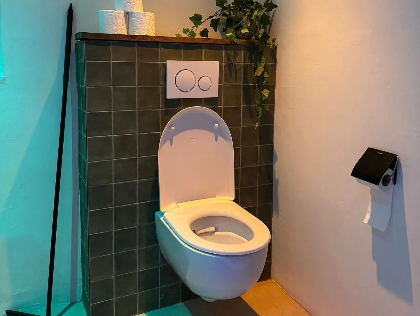 Modern bathroom design with a wall-mounted toilet, green tiles, and decorative plants.