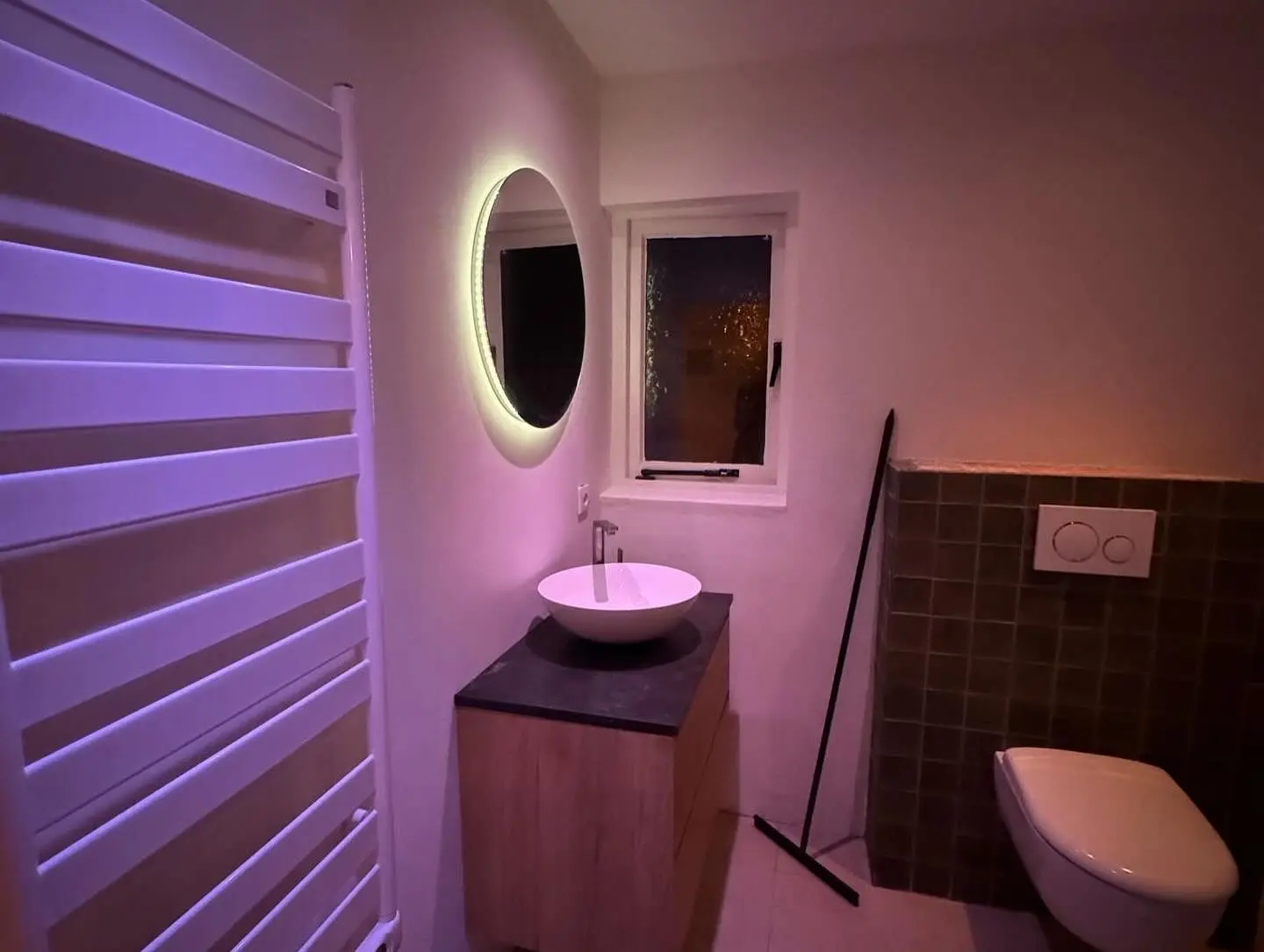 Full view of the bathroom with a heated towel rack, illuminated mirror, and a modern toilet setup.