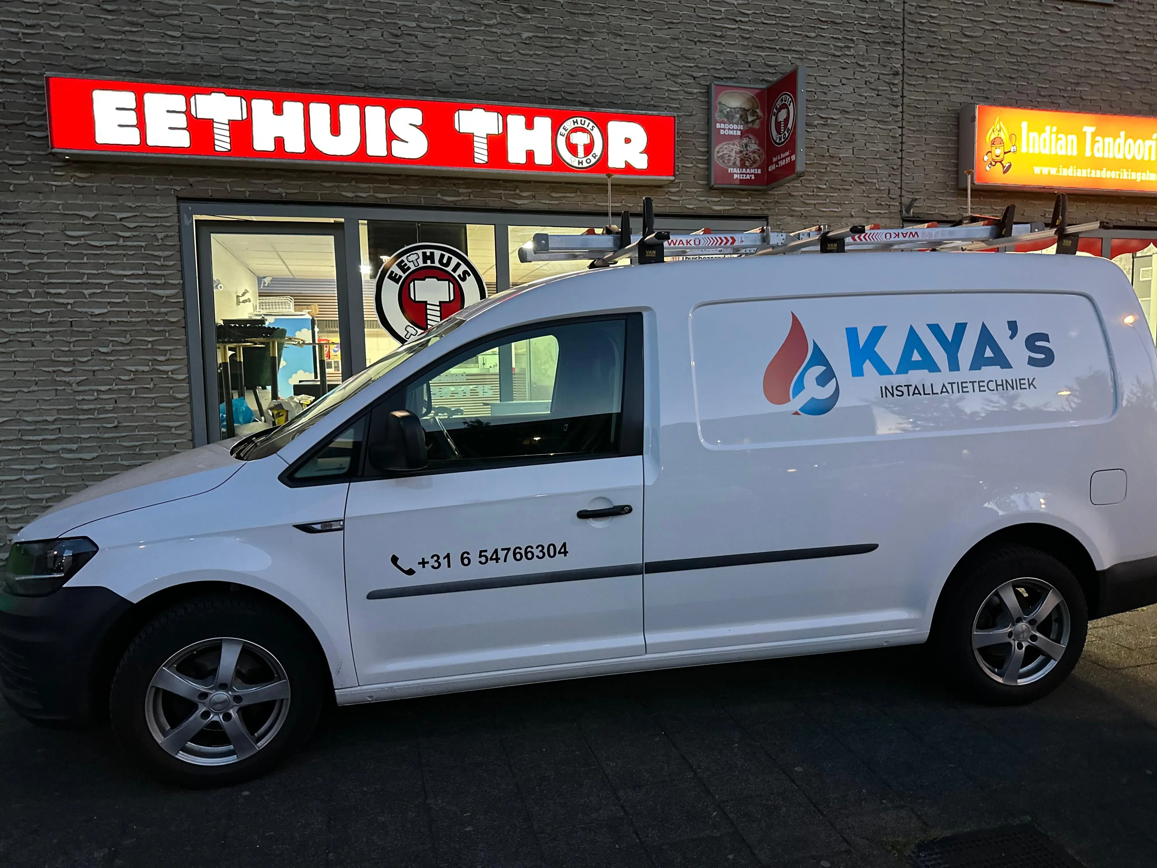 A plumber’s van with the company logo and contact information, parked in front of a residential building.