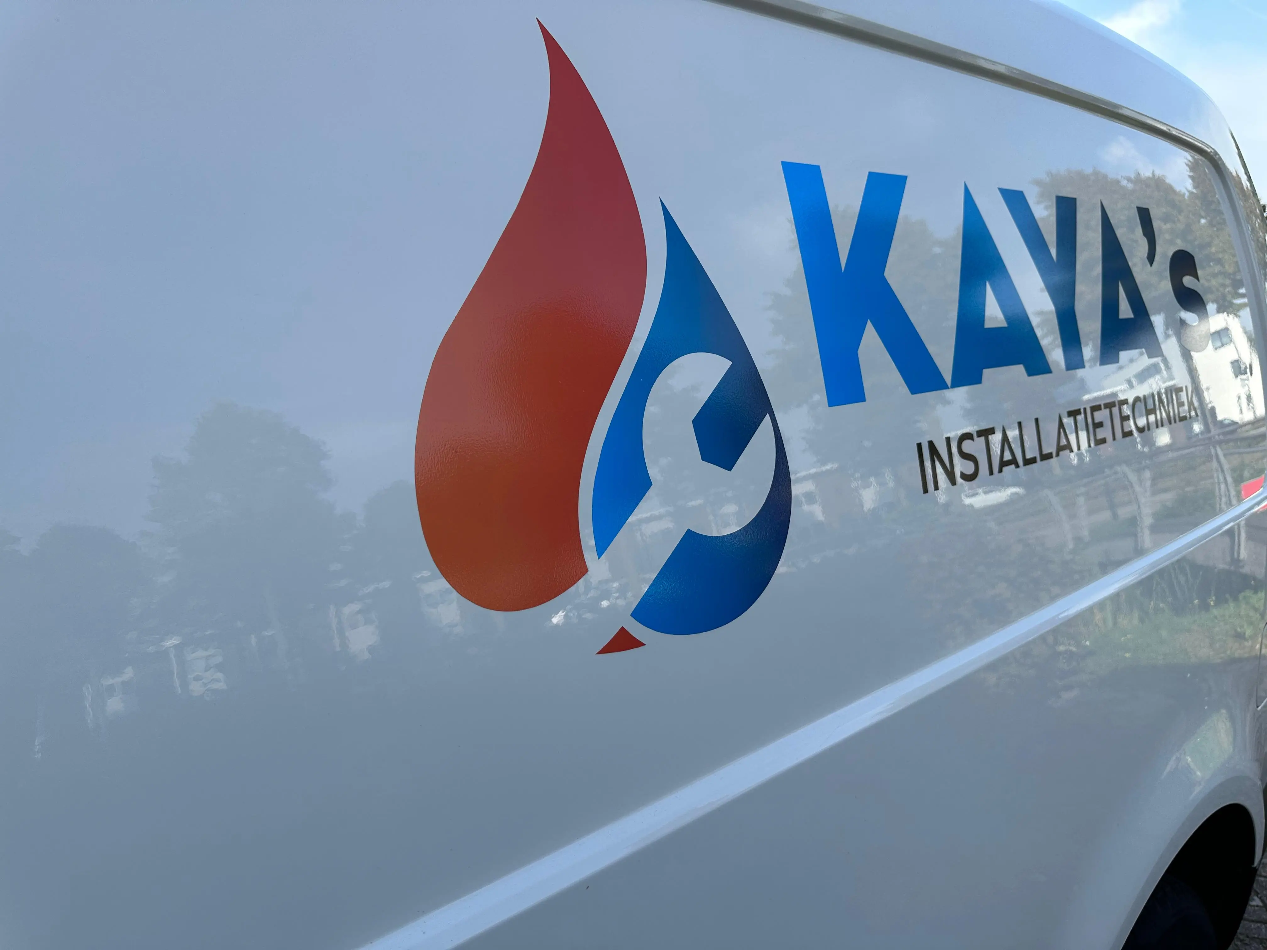 A plumber’s van with the company logo and contact information, parked in front of a residential building.